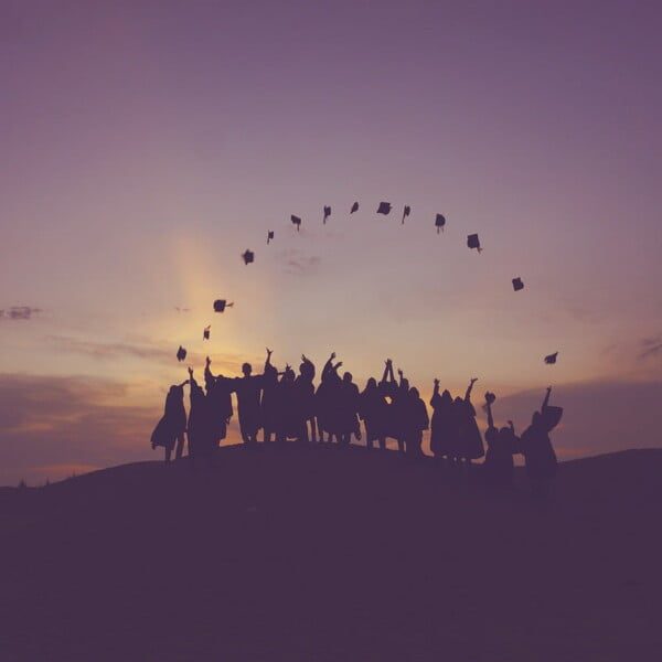 Timeless Graduation Outfit Ideas & Tips For Women over 40 14 Silhouetted graduates in stylish graduation outfits stand on a hill at sunset, joyfully tossing their caps into the air against a colorful sky.