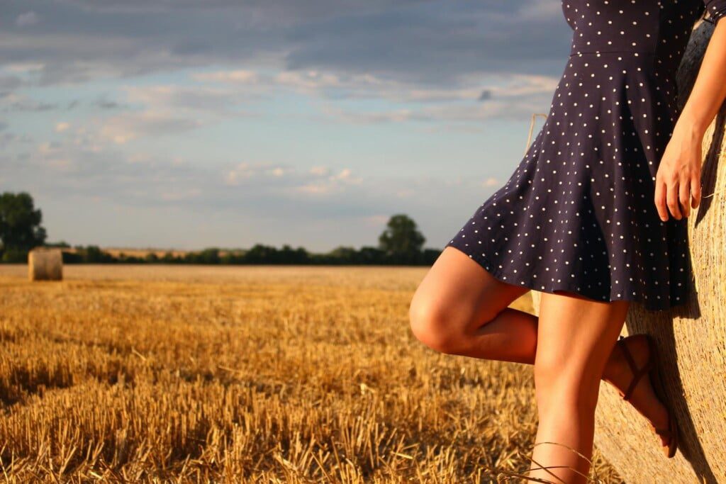 A person in a navy polka dot dress leans against a hay bale in a sunlit field, showcasing their summer fashion haul. The sky is partly cloudy, and more hay bales are scattered in the background, creating the perfect Abercrombie-inspired scene.