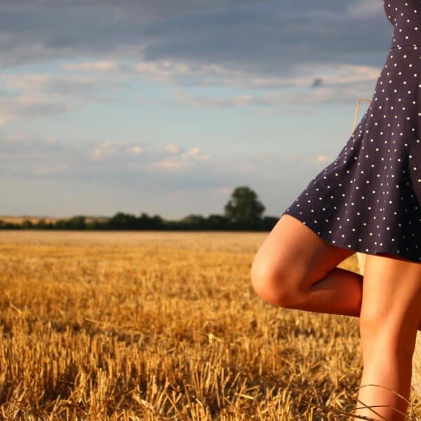 Summer Haul ABERCROMBIE : 5 DRESSES YOU SHOULD GET THIS SUMMER 18 A person in a navy polka dot dress leans against a hay bale in a sunlit field, showcasing their summer fashion haul. The sky is partly cloudy, and more hay bales are scattered in the background, creating the perfect Abercrombie-inspired scene.