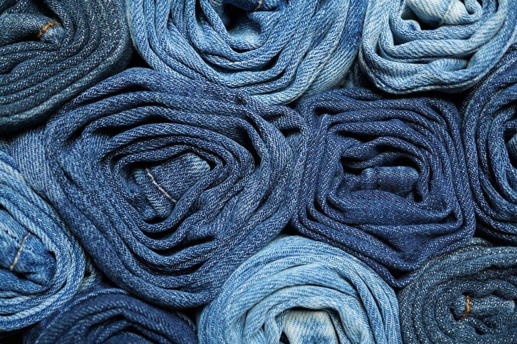 Rolled-up denim jeans arranged closely together, forming a textured pattern. The jeans vary in shades of blue, from light to dark, showcasing the different hues of denim fabric. A versatile choice for fashion tips on wide leg jeans that can flatter any silhouette, especially over 40.