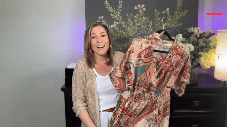 Shein Summer Dresses: Your Ultimate Summer Fashion Guide 1 A woman smiles and holds up a colorful, patterned dress on a hanger. Shes standing in a room with a floral wall pattern and soft lighting from a lamp, capturing the essence of summer fashion. She wears a light sweater over a white outfit, embodying the latest trends in Shein Summer Dresses.