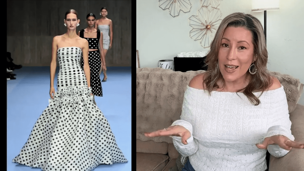 A woman in an off-shoulder sweater sits on a sofa, gesturing animatedly. On the left, a runway with models in polka dot dresses. The setting is a modern, stylish room with wall decor.